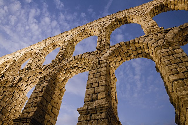 The aqueduct in Segovia looms overhead, with blue sky and clouds