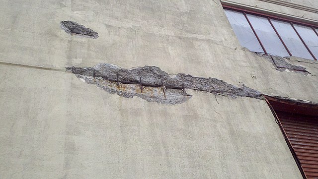 A close-up of spalling concrete. Bits of concrete have flaked away, exposing rebar.