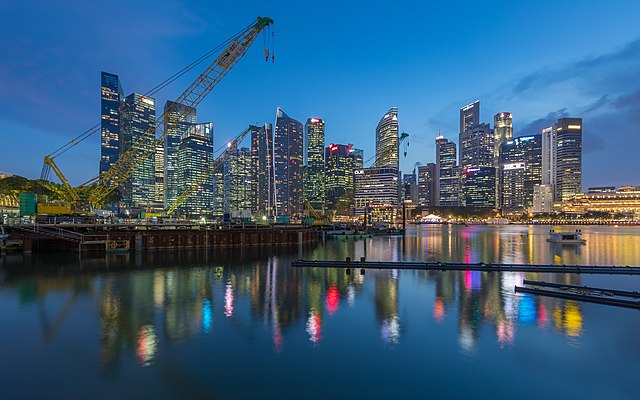 Crane and skylines of the Central Business District reflecting in the water at blue hour in Singapore.