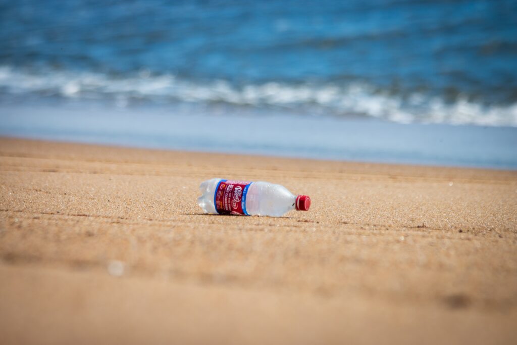 Empty soda bottle on sandy beach, symbolizing the global issue of plastic and microplastic pollution, and its devastating impact on marine life.