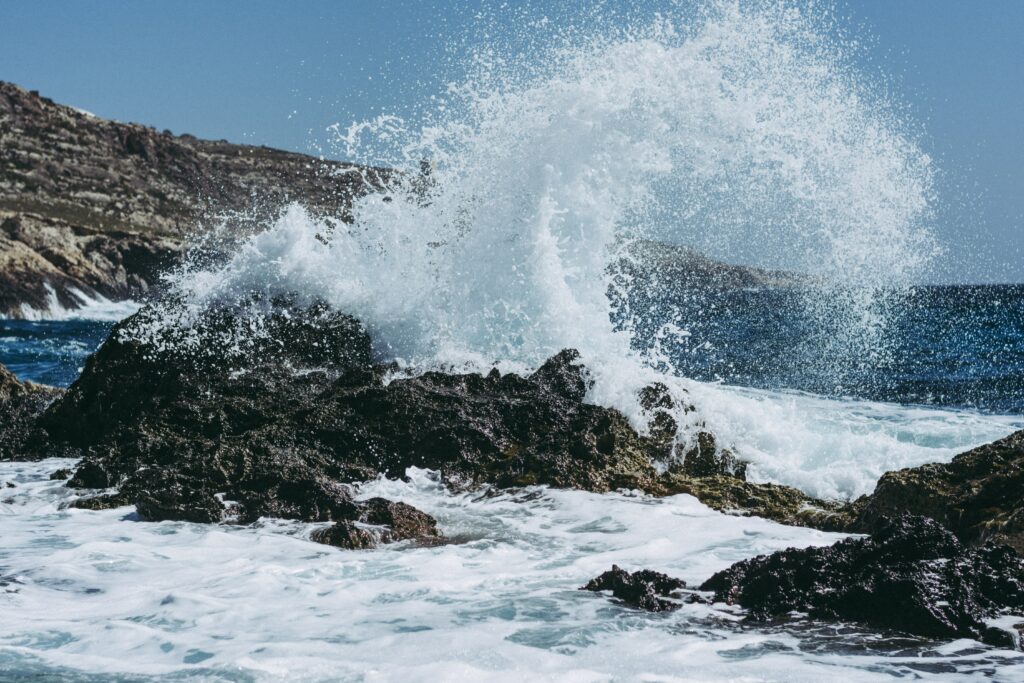 Powerful wave crashing into jagged rocks, sending spray embedded with microplastics high into the air. Whipped by sea breezes, these plastics become airborne.